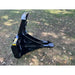 Black steel tree puller attachment with serrated jaw and triangular frame resting on grass with scattered leaves