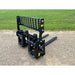 Black steel skid steer forks with perforated vertical backrest and two flat extended tines on gravel and grass background
