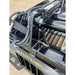 Close-up of black steel rock grapple attachment hinge area with hydraulic cylinder, hoses, and welds on concrete surface