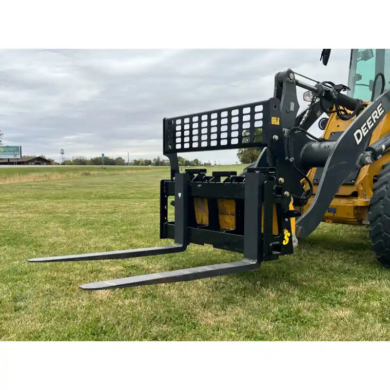 Black steel pallet fork attachment with perforated mesh backrest and two extended fork tines on grassy field