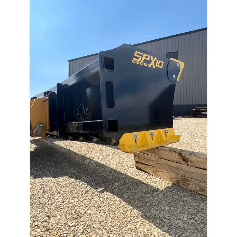 Black steel skid steer attachment with yellow cutting edge and mounting plate on gravel surface near building