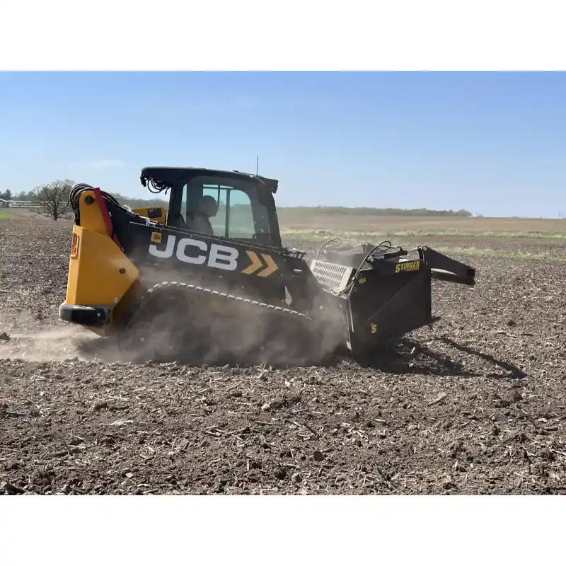 Side view of yellow and black tracked skid steer with rock reel attachment tilling dry soil in open field