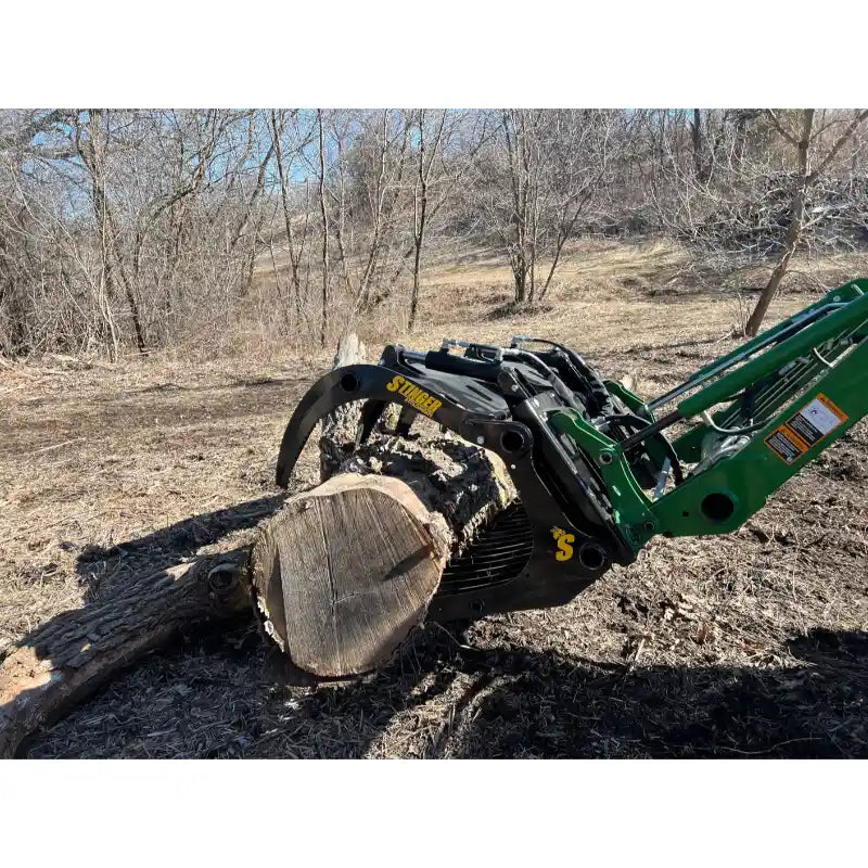 Green loader arm with black steel log grapple attachment holding large cut tree log on bare soil