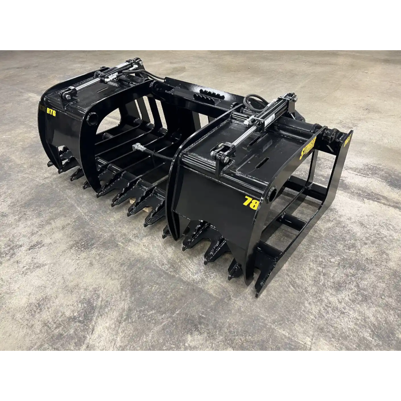 Black metal skid steer grapple attachment with dual hydraulic cylinders, thick curved tines, and reinforced crossbars on concrete floor