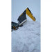 Black and yellow skid steer snow pusher blade lifting a large pile of snow under overcast sky