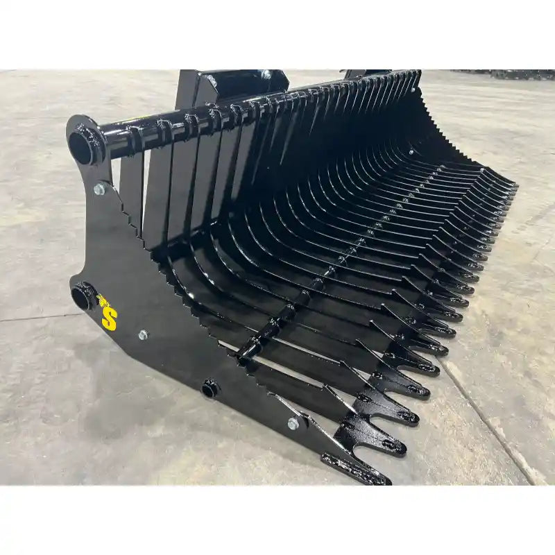 Black metal rock bucket attachment with narrow spaced curved tines and reinforced side panels on concrete floor