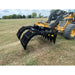 Yellow Deere skid steer equipped with black steel rake-style attachment over grassy field under cloudy sky