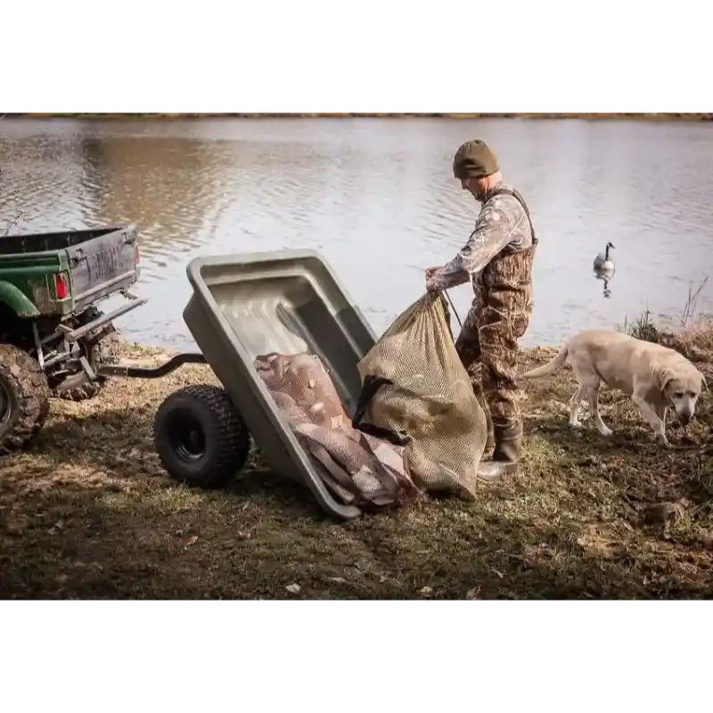 Utility vehicle hitched to Swisher 16 cu ft poly cart tilted dumping fish near water with man and dog, gallery 1