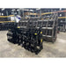 Two black tractor clam grapple attachments placed on concrete floor in a warehouse with metal racks in background