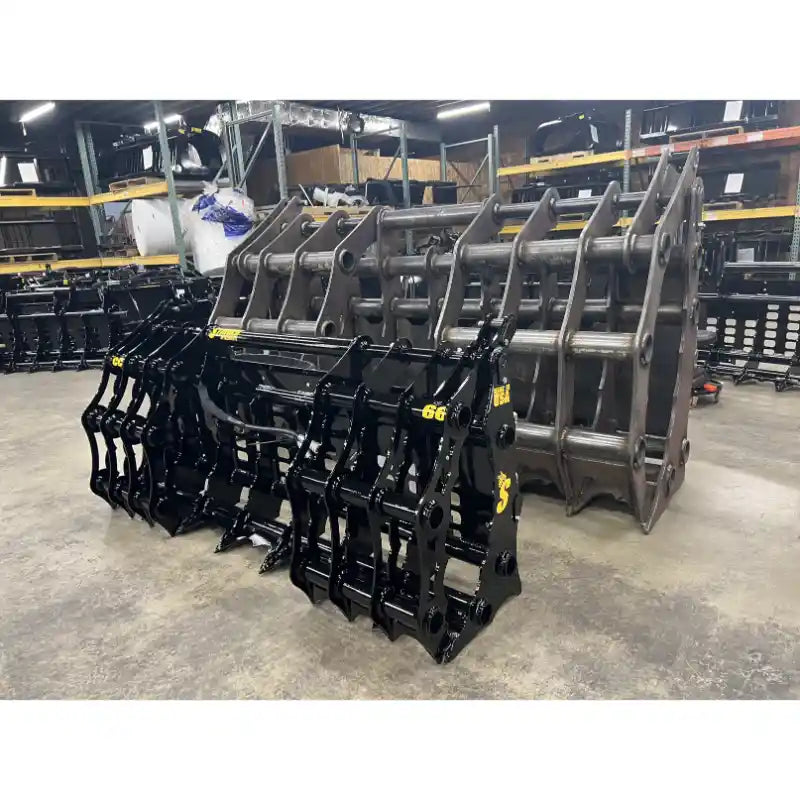 Two black tractor clam grapple attachments placed on concrete floor in a warehouse with metal racks in background