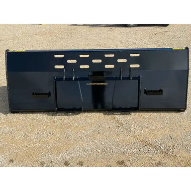 Wide black steel snow bucket attachment with mounting brackets and vent slots on gravel surface