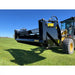 Front-left angled view of skid steer with black rock bucket reel attachment over green grass under blue sky