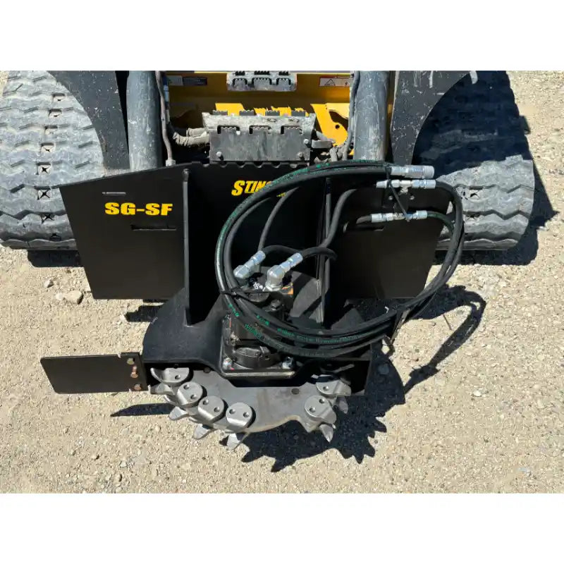 Stump grinder attachment with cutting teeth, hydraulic hoses, and black steel mounting frame on tracked loader platform