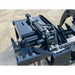 Close-up of black metal skid steer hydraulic grapple attachment with hoses, cylinders, and mounting bracket on gravel surface