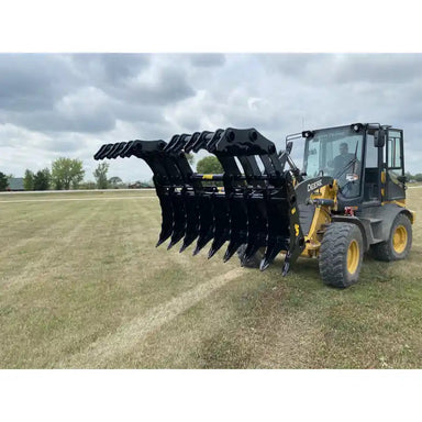 Front loader tractor with large black steel claw-style grapple attachment open over mowed grassy field under cloudy sky