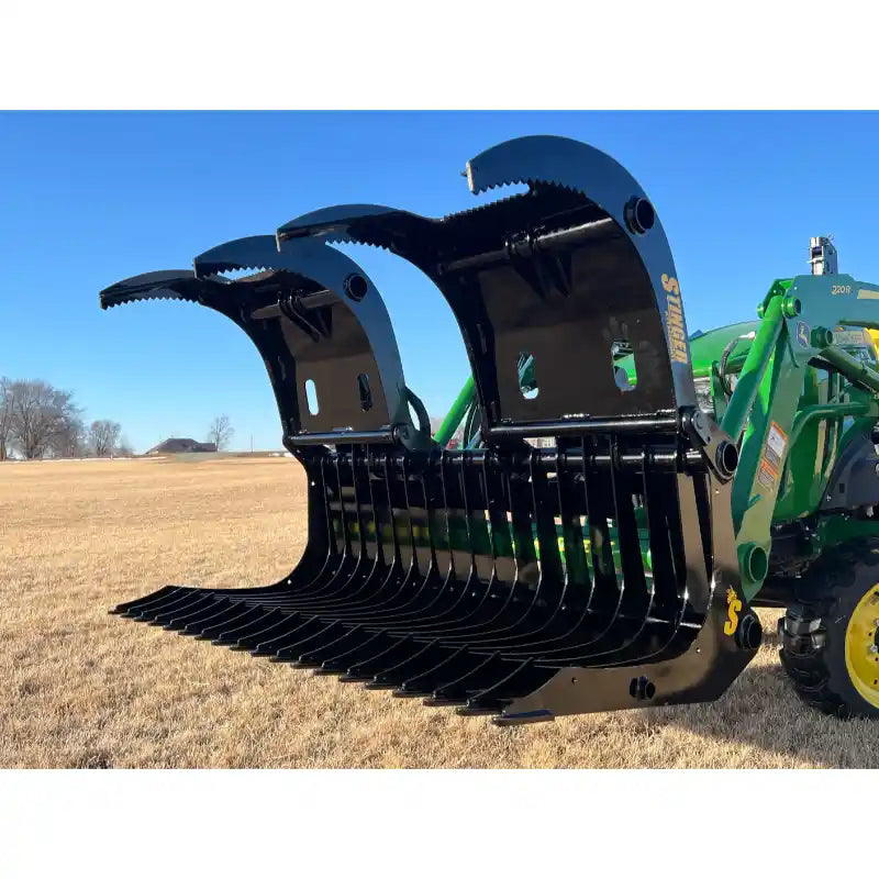 Black steel rock grapple with serrated curved jaws and curved tines mounted on green tractor loader arm outdoors