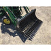 Black metal rock bucket attachment with spaced curved tines mounted on green loader arm over gravel ground