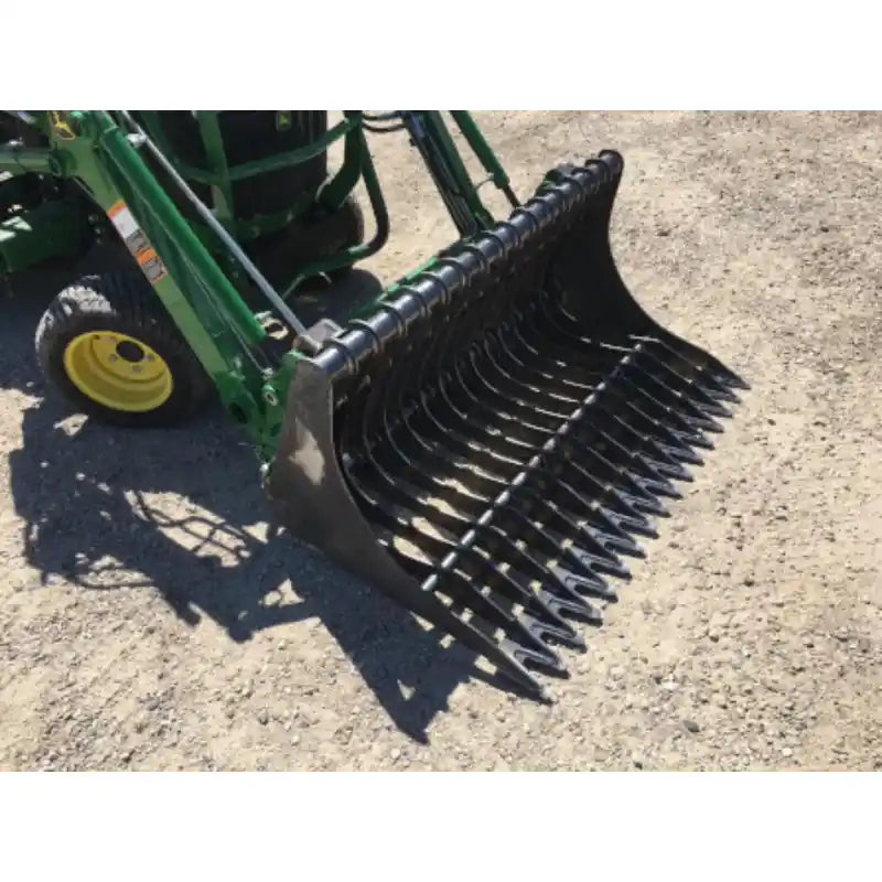 Black metal rock bucket attachment with spaced curved tines mounted on green loader arm over gravel ground