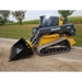 Yellow and gray compact track loader with toothed black bucket attachment on gravel path near grass and trees