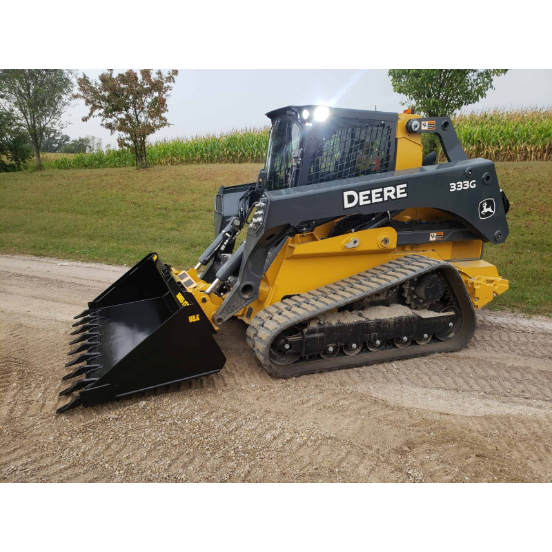 Yellow and gray compact track loader with toothed black bucket attachment on gravel path near grass and trees