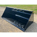 Wide black steel snow bucket attachment with angled sides, bolt-on cutting edge, and ventilation slots on gravel surface