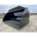 Front-right angled view of a black steel construction bucket attachment with reinforced cutting edge on gravel ground