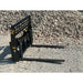 Black steel compact pallet fork attachment with welded grid backrest and two extended fork tines on gravel ground outdoors