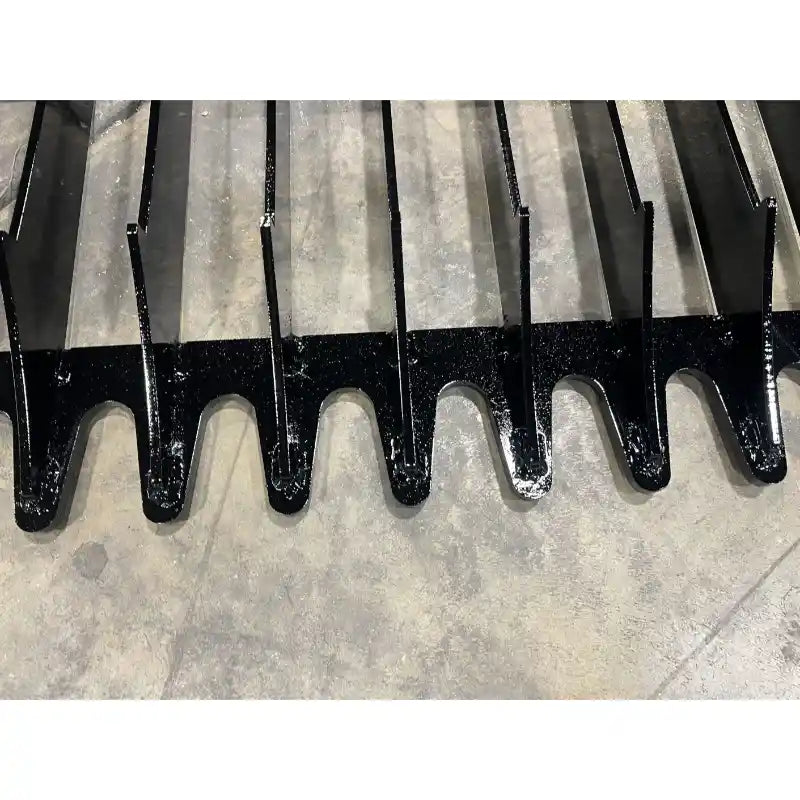 Close-up of black metal bucket attachment with narrow spaced flat tines on concrete floor surface