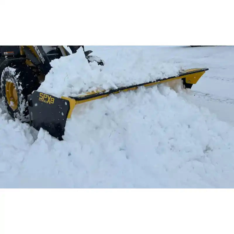 Yellow and black skid steer snow pusher attachment clearing a heavy layer of snow on paved surface