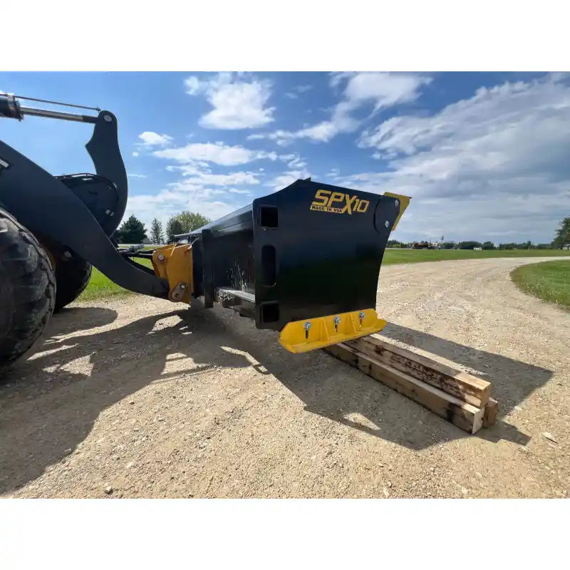 Black steel skid steer snow pusher attachment with yellow bolt-on cutting edge on gravel driveway under blue sky