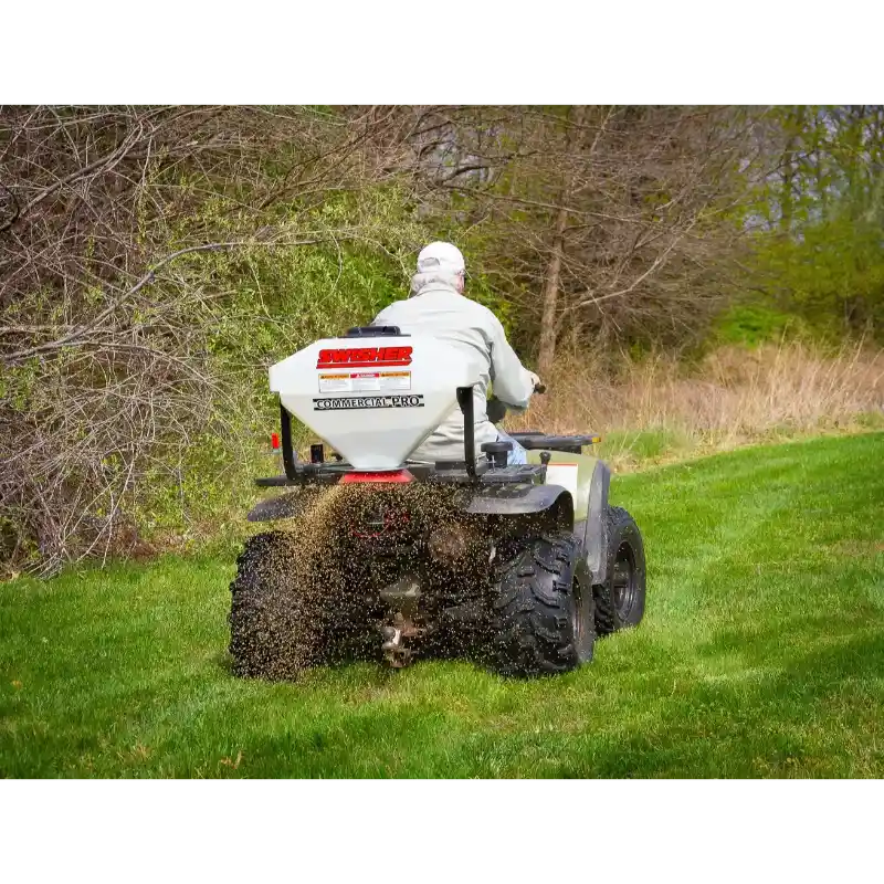 Rear view of Swisher ATV Commercial Pro Spreader mounted on ATV dispersing material across grassy area, gallery position 1