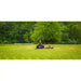 Zero-turn mower cutting a grassy field with trees in the background, mower centered, gallery position 1