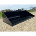Black skid steer material bucket with smooth interior and yellow Stinger Series 3 label on gravel surface outdoors