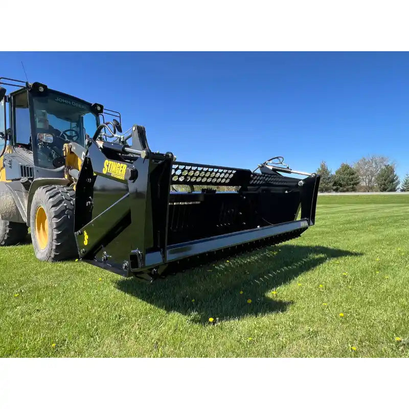 Front-left angled view of tractor with black rock bucket reel attachment on green grassy field under clear blue sky
