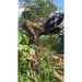 Black steel clam grapple attachment lifting large uprooted tree stump with roots amid green vegetation