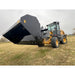 Yellow loader with black hydraulic dump bucket attachment raised over grassy field under overcast sky