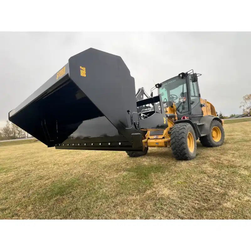 Yellow loader with black hydraulic dump bucket attachment raised over grassy field under overcast sky