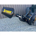 Black Stinger mixing drum attachment connected to skid steer loader arm over gravel surface near metal wall