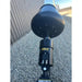 Black Stinger concrete mixer attachment with hydraulic fittings mounted on loader arm over gravel near metal building wall