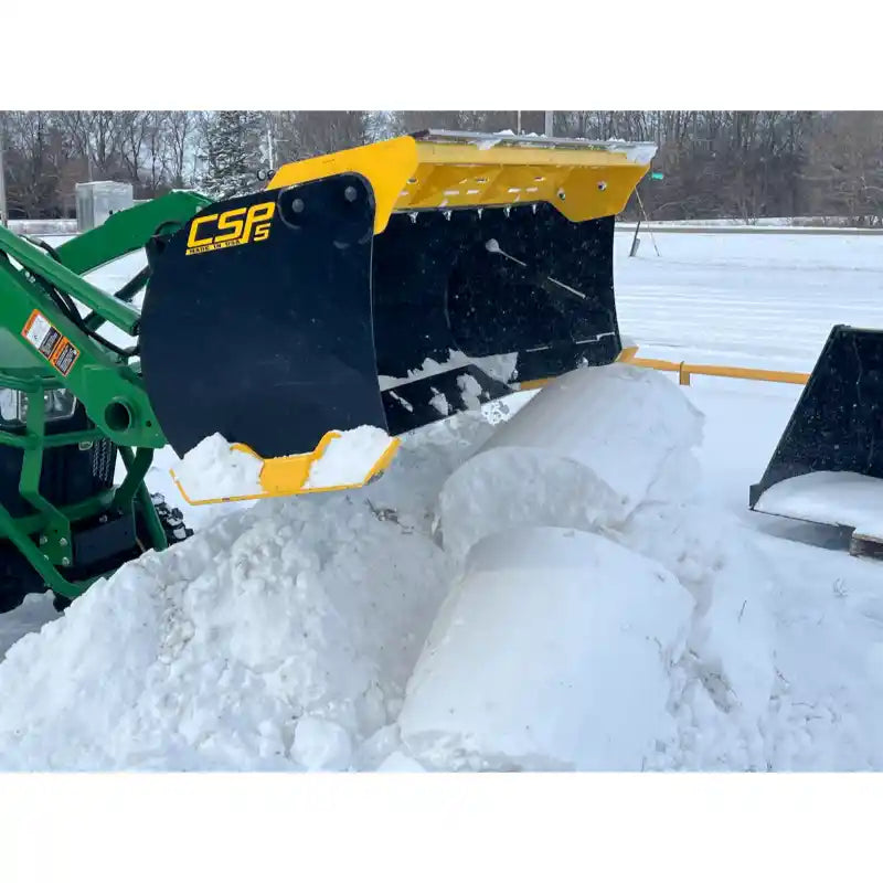Black and yellow steel snow pusher attachment lifting rolled snow, mounted on green loader in snowy outdoor area