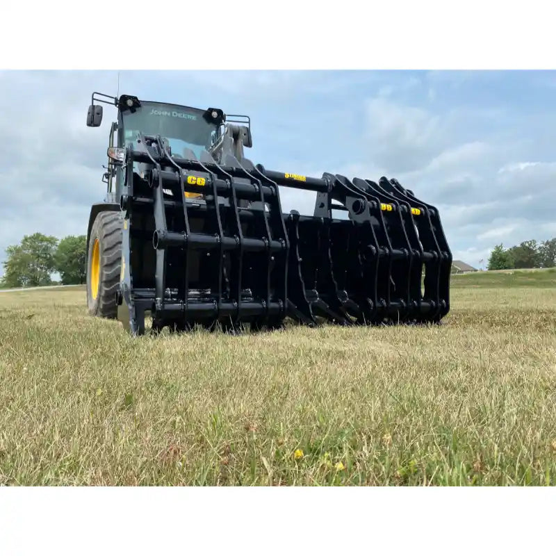 Front view of black steel clam-style grapple attachment mounted on yellow loader over grassy field under cloudy sky
