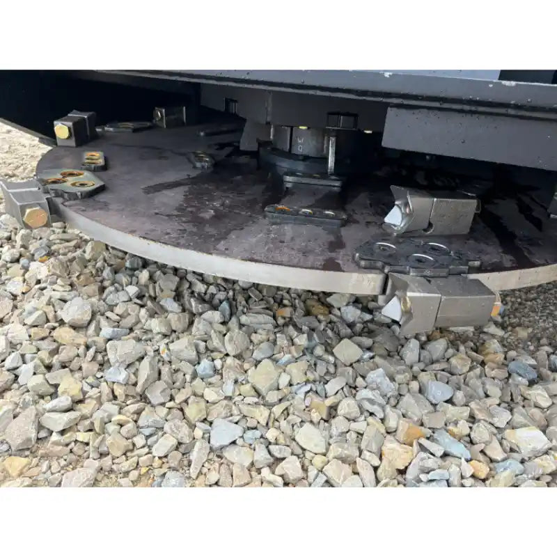 Close-up of underside steel rotary mulcher disc with cutting teeth and mounting bolts resting on gravel surface