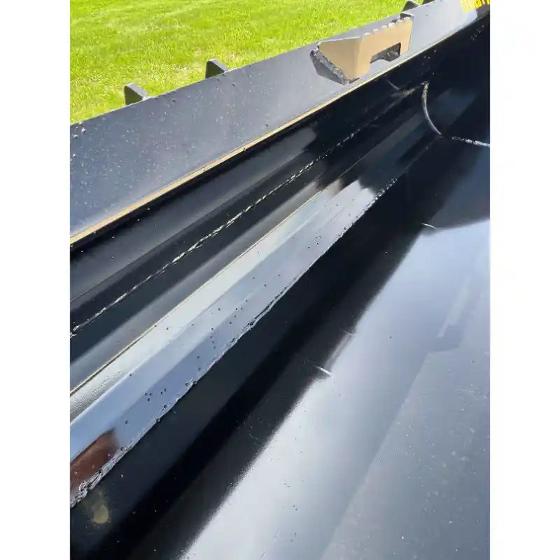 Close-up of inside black steel skid steer material bucket showing weld seams and reinforced edges outdoors