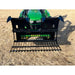 Front view of black metal rock grapple attachment with spaced flat tines mounted on green compact tractor