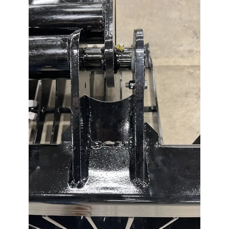 Close-up of black painted steel hinge bracket with visible welds and pin connection on skid steer attachment
