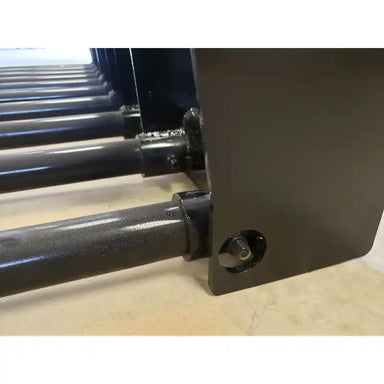 Close-up of black painted steel manure tine bucket attachment with bolt fastened mounting plate on concrete floor indoors