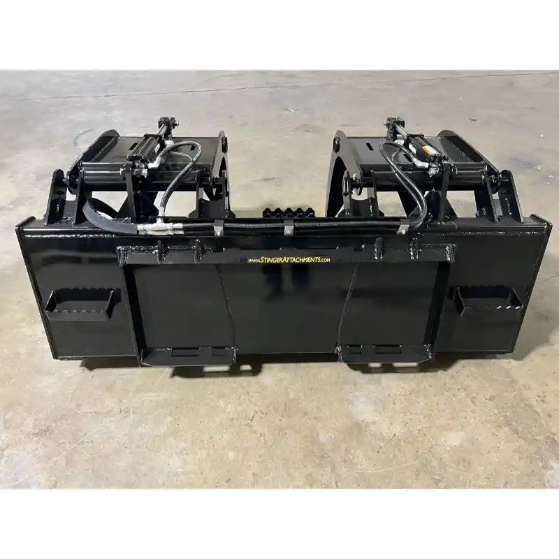 Black metal grapple bucket attachment with dual hydraulic cylinders and mounting brackets on indoor concrete floor