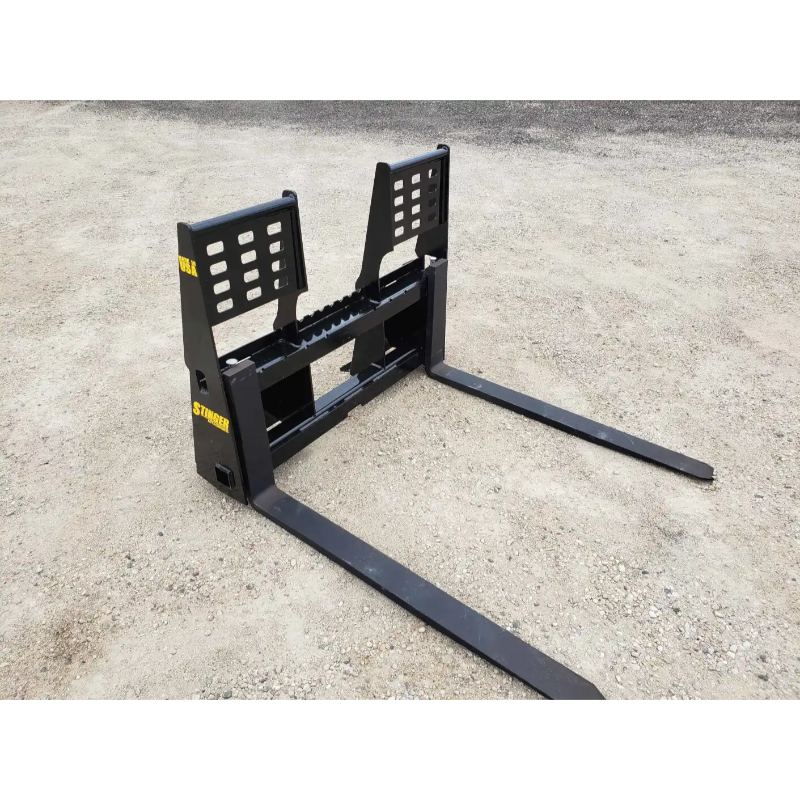 Black steel pallet fork attachment with two long horizontal tines and perforated vertical backrest on dirt ground