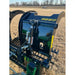 Black steel compact rock grapple attachment with serrated clamshell jaws and hydraulic hoses over dry grass