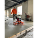 Concrete power trowel with white fuel tank and red engine operated by worker wearing orange shirt on wet concrete floor